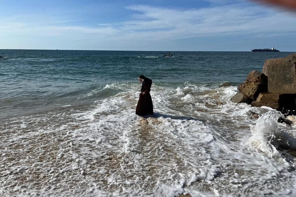 La foto ritrae una monaca europea sorpresa da un’ondata imprevista su una costa Africana